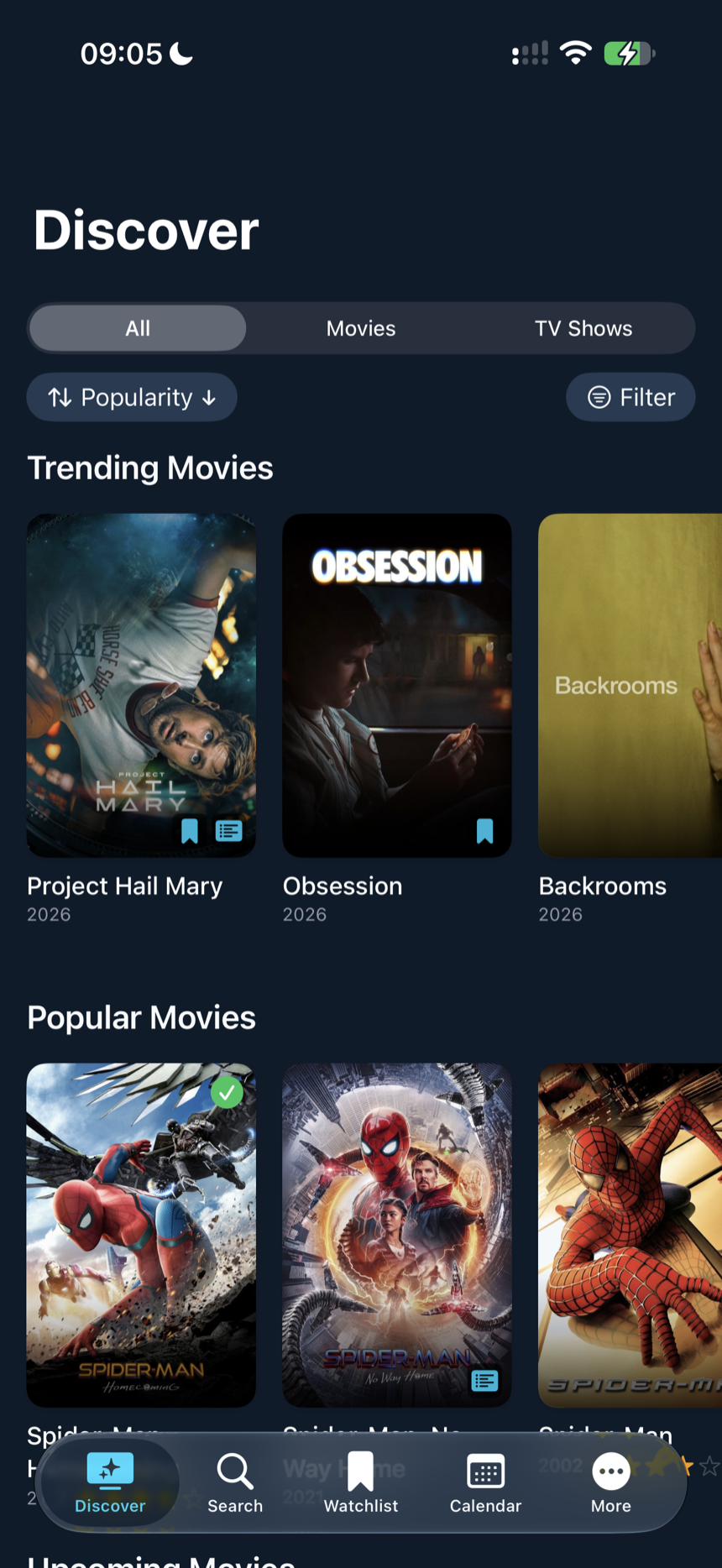 The Discover tab on iPhone: trending and popular films in a poster grid, with small badges marking the ones already on the watchlist or watched.